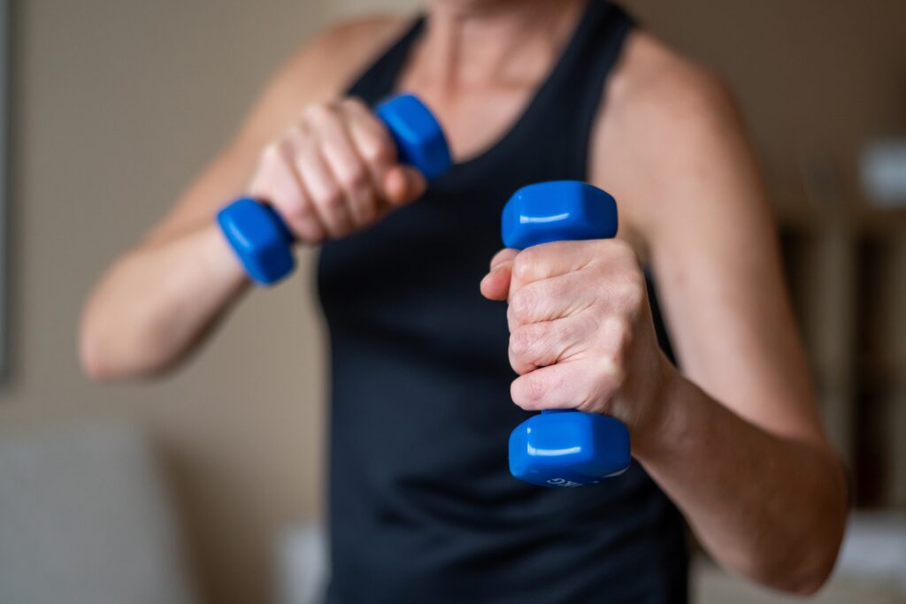 Close-up of a midlife woman holding dumbbells during a strength training workout to support muscle and metabolism