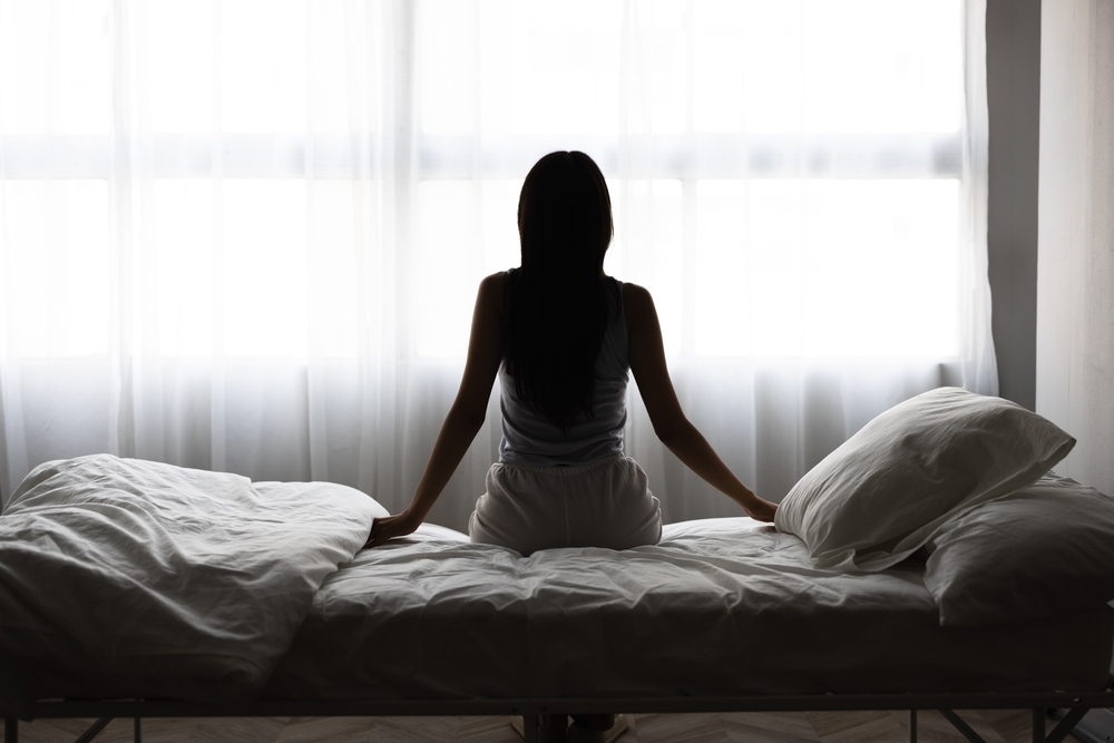 Silhouette of a woman sitting on the edge of her bed in soft morning light, representing the persistent, unexplained fatigue many women experience in perimenopause.