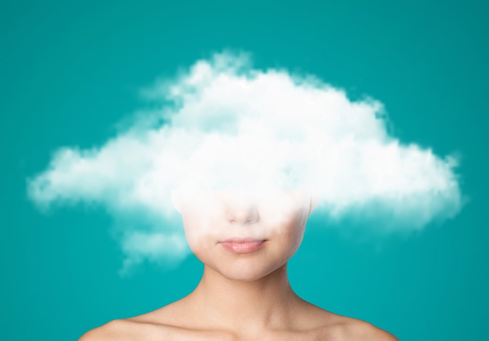 Midlife woman with her head partly obscured by soft clouds, illustrating brain fog.